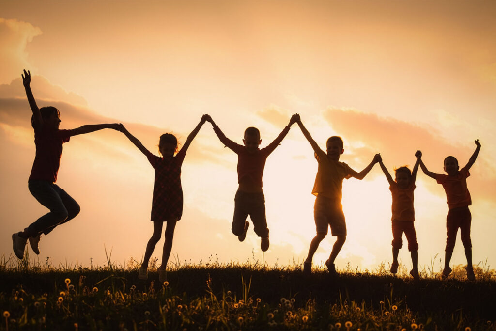 Silhouettes of children jumping hand in hand at sunset, showing normal childhood variance